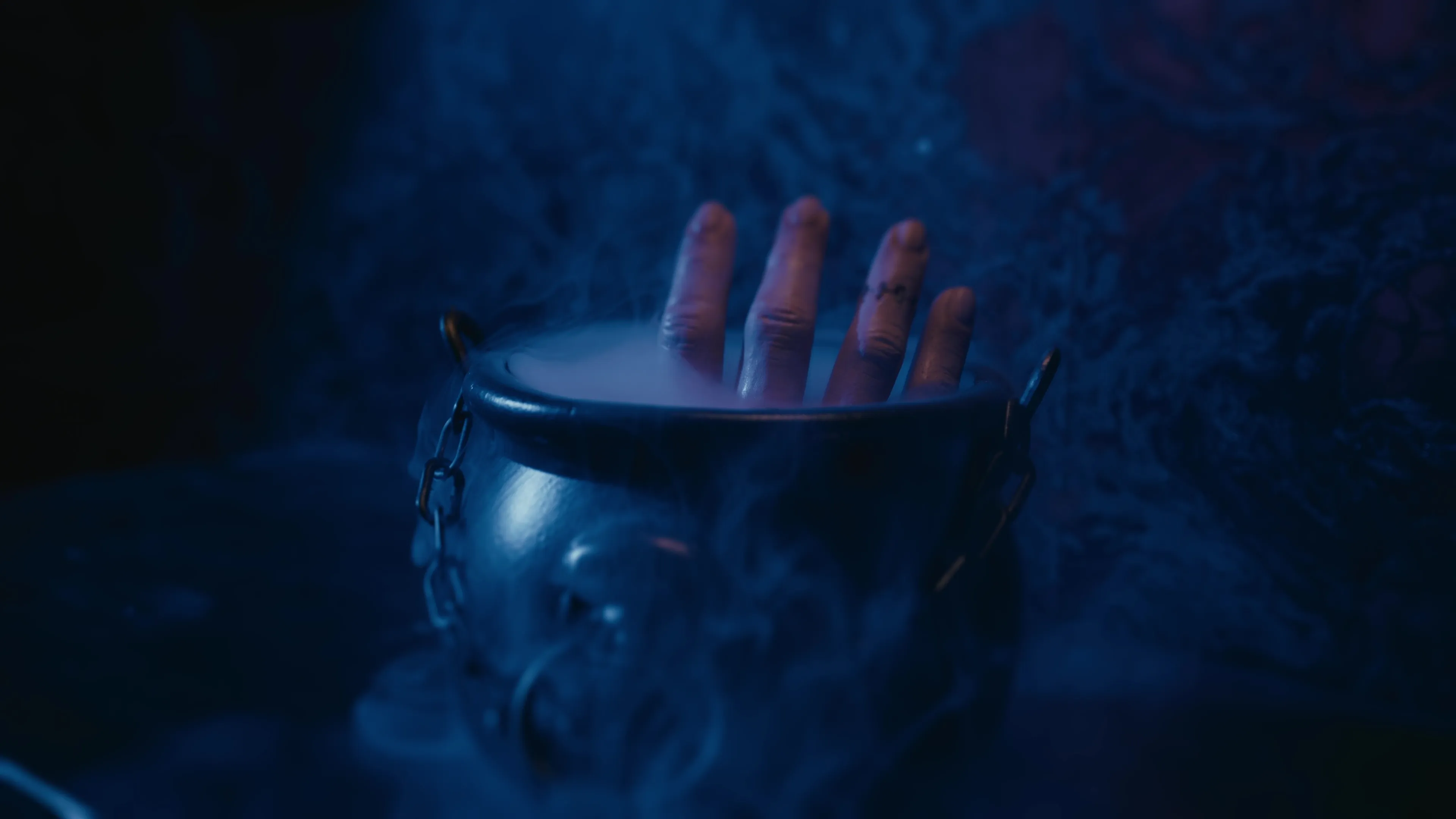 Eine Hand greift aus einem rauchenden Kessel in tiefblauem Licht