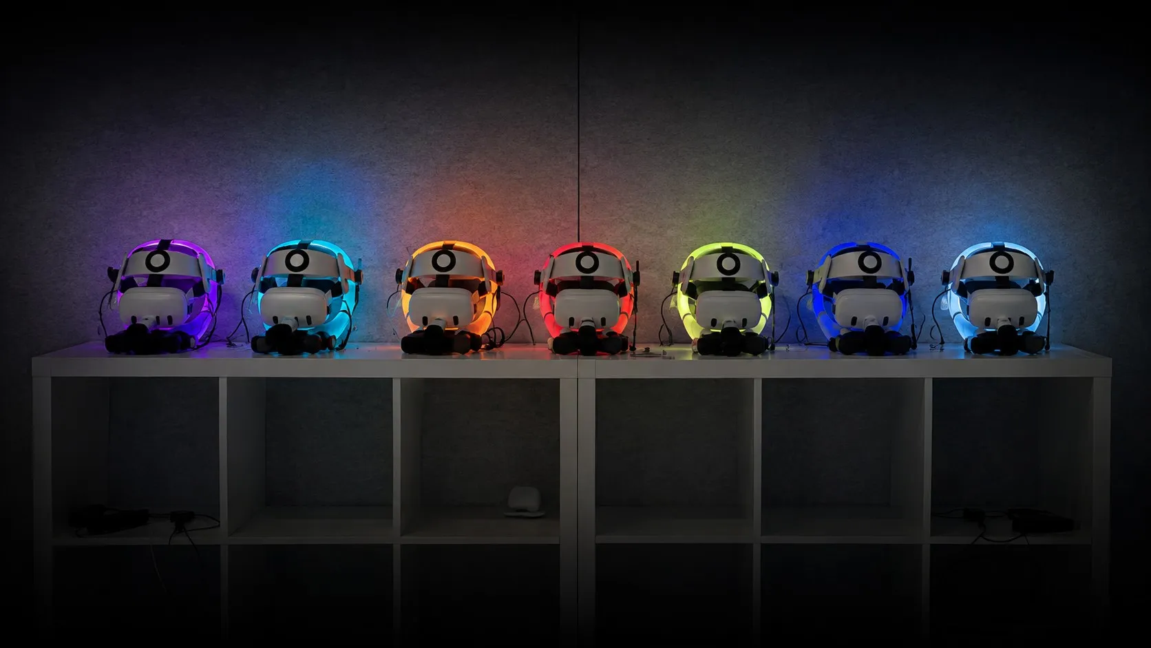 Sieben VR-Headsets auf einem Regal, jedes in einer anderen Farbe beleuchtet, dunkler Raum