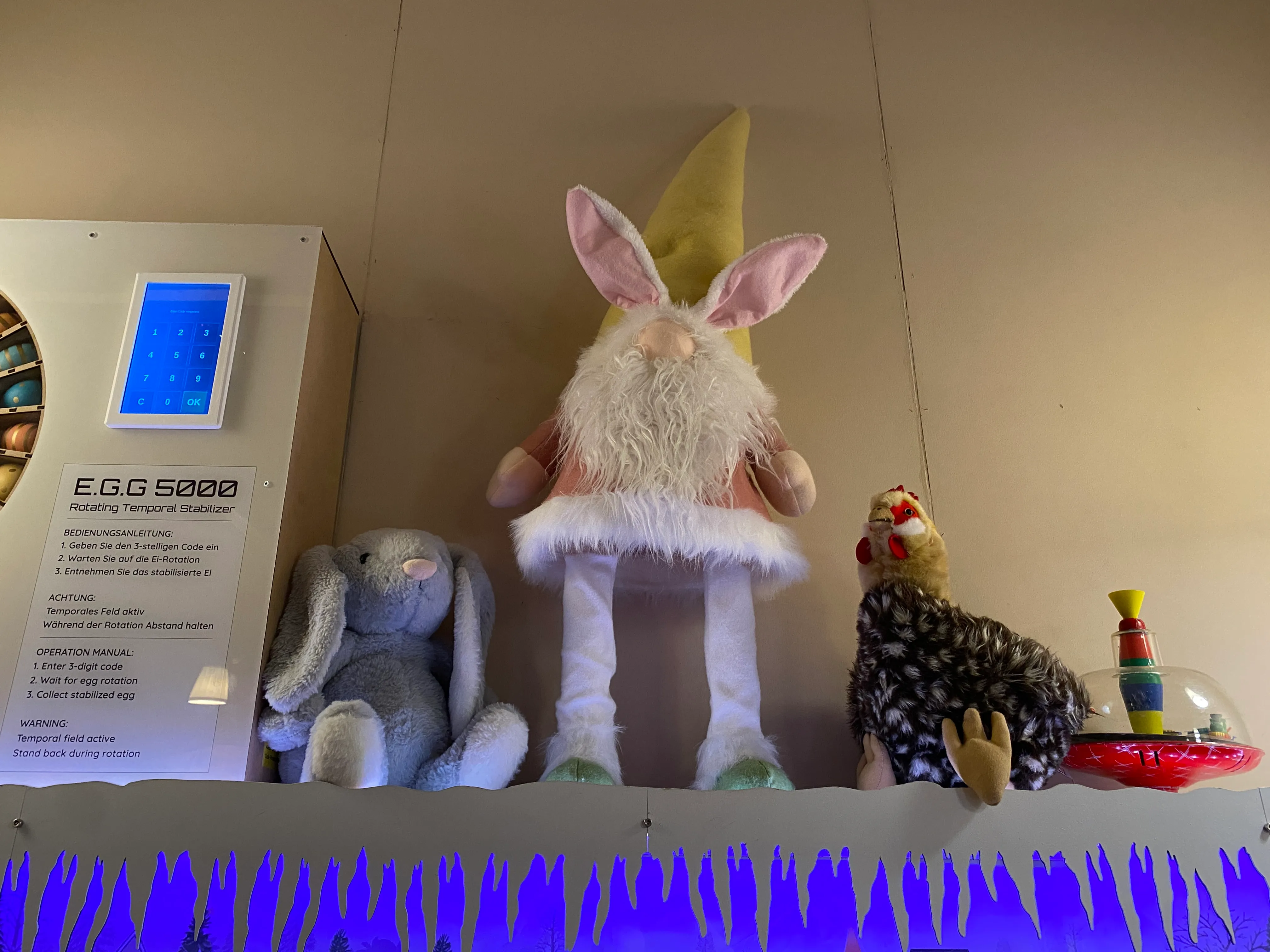 Regal mit Plüschtieren Hasi, Willi Wichtel und Huhn Hildebertha neben dem E.G.G. 5000 — blaue Bodenbeleuchtung